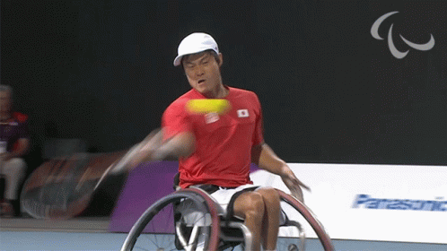 A Man In A Wheelchair Swings A Tennis Racket At A Tennis Ball GIF