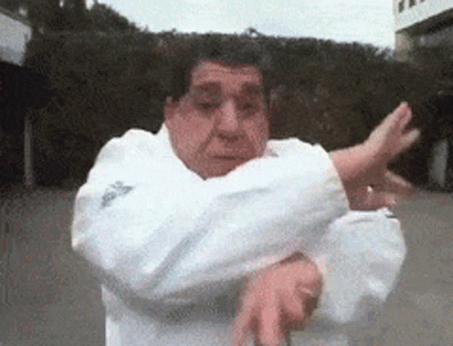 A Man In A White Adidas Jacket Is Doing A Karate Move GIF