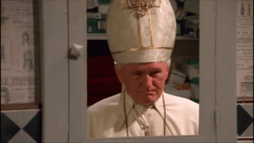A Man In A White And Gold Hat Is Looking Out Of A Window GIF