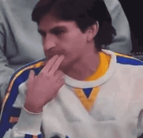 A Man In A White And Yellow Sweater Is Sitting In A Chair With His Hand On His Chin . GIF