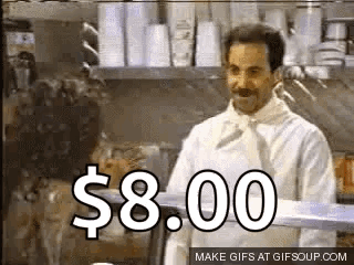 A Man In A White Chef 'S Coat Is Standing In A Kitchen With A Sign That Says $ 8.00 On It . GIF