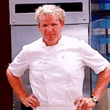 A Man In A White Chef 'S Jacket Is Standing With His Hands On His Hips In Front Of A Refrigerator . GIF