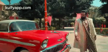 A Man In A White Coat And A Beard Is Standing Next To A Red Car . GIF