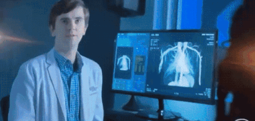 A Man In A White Coat Is Standing In Front Of A Computer Monitor . GIF
