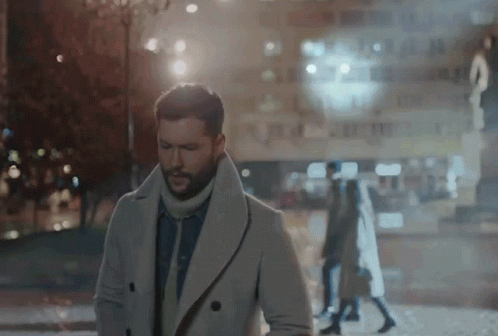 A Man In A White Coat Is Walking Down The Street GIF