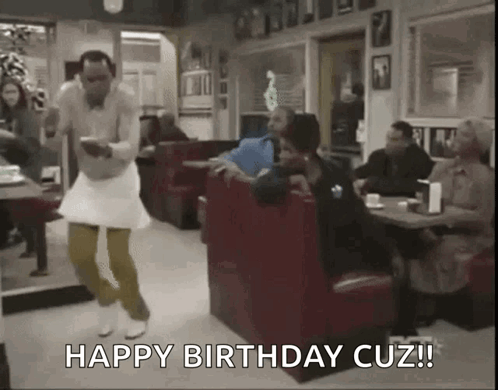 A Man In A White Dress Is Dancing In A Diner While A Woman Sits At A Table . GIF