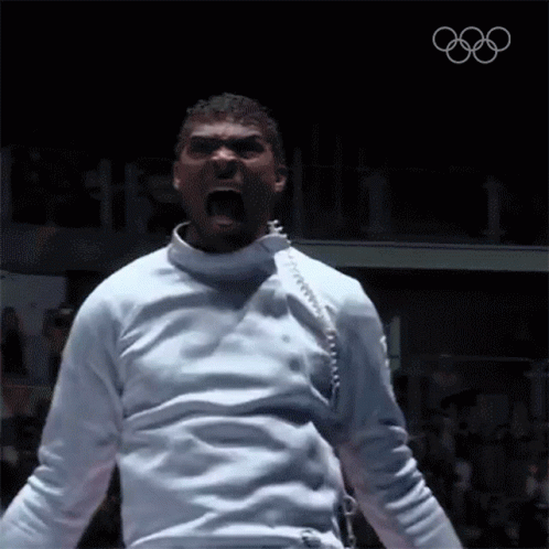 A Man In A White Fencing Uniform Is Screaming With The Olympics Logo In The Background GIF