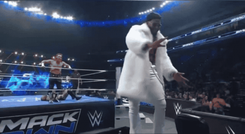 A Man In A White Fur Coat Is Dancing In Front Of A Mack W Sign GIF