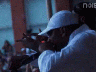 A Man In A White Hat Is Singing Into A Microphone In Front Of A Crowd And The Word Noise Is Visible In The Corner GIF