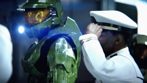 A Man In A White Hat Salutes Another Man In A Green Suit GIF