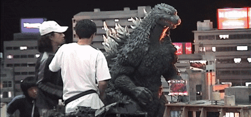 A Man In A White Hat Stands In Front Of A Giant Monster GIF