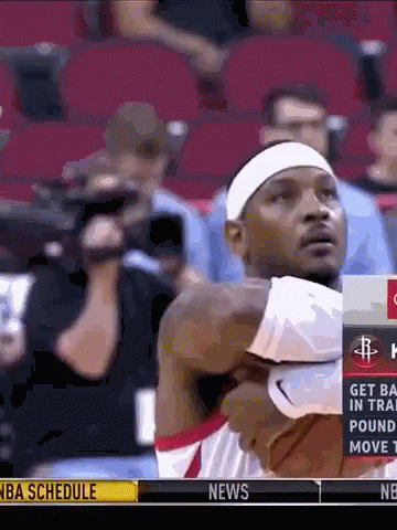 A Man In A White Headband Is Holding A Basketball In Front Of A Nba Schedule Advertisement GIF
