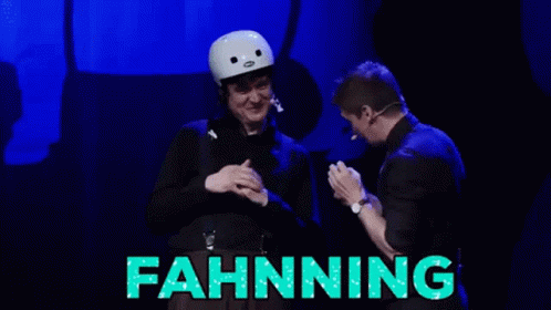 A Man In A White Helmet Stands Next To A Man In A Black Suit With The Word Fahnning Written In Green GIF
