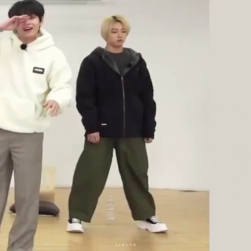 A Man In A White Hoodie And A Man In A Black Jacket Are Standing Next To Each Other On A Wooden Floor . GIF