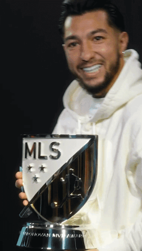 A Man In A White Hoodie Holds A Trophy That Says Mls GIF