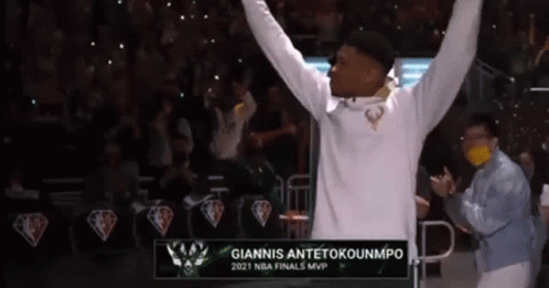A Man In A White Hoodie Is Raising His Arms In The Air In Front Of A Crowd . GIF