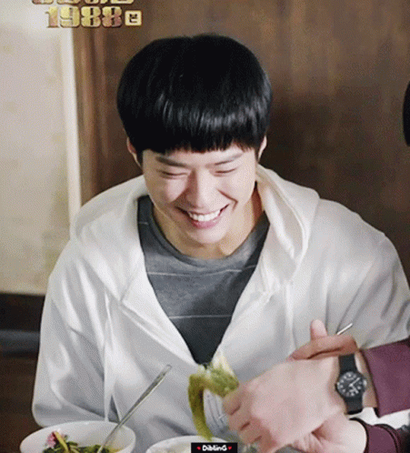 A Man In A White Hoodie Is Smiling While Eating A Meal GIF