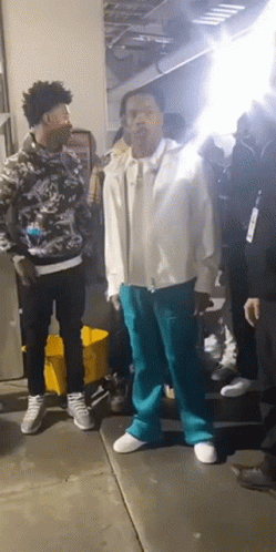 A Man In A White Jacket And Blue Pants Is Standing In A Crowd Of People GIF