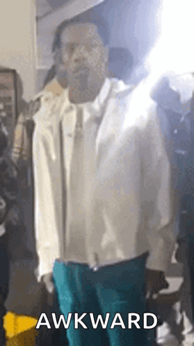 A Man In A White Jacket And Blue Pants Is Standing In Front Of A Crowd With The Word Awkward On The Bottom . GIF