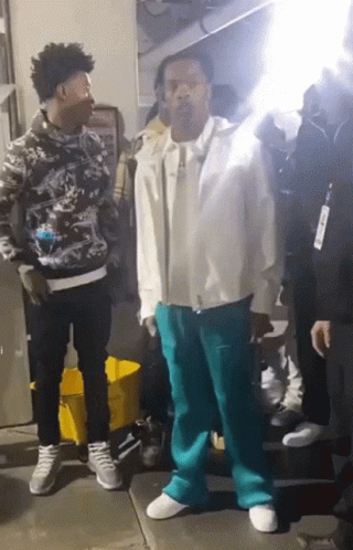 A Man In A White Jacket And Blue Pants Is Standing Next To Another Man GIF