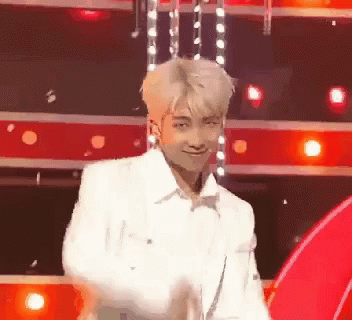 A Man In A White Jacket Is Dancing On A Stage In Front Of Red Lights . GIF