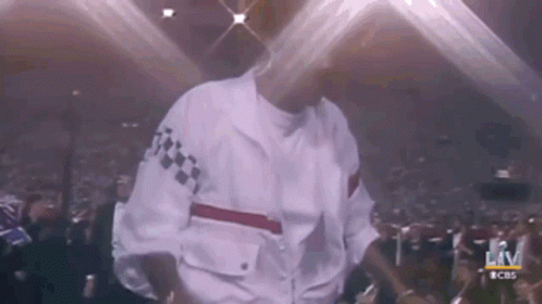 A Man In A White Jacket Is Dancing On Stage In Front Of A Crowd . GIF