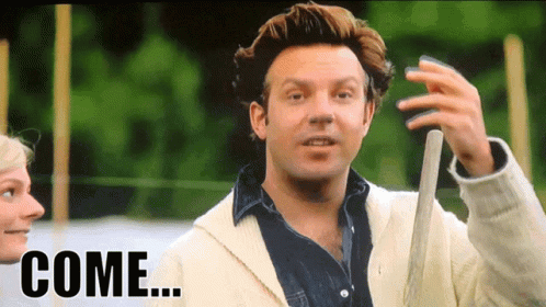 a man in a white jacket is holding a baseball bat and the word come is on the screen behind him
