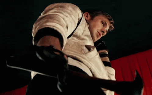 A Man In A White Jacket Is Holding A Hammer In Front Of A Red Curtain GIF