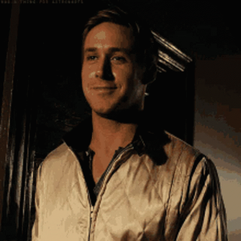 A Man In A White Jacket Is Smiling In Front Of A Black Wall GIF