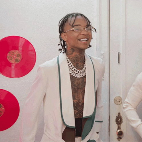 A Man In A White Jacket Is Smiling In Front Of A Wall With Red Records GIF