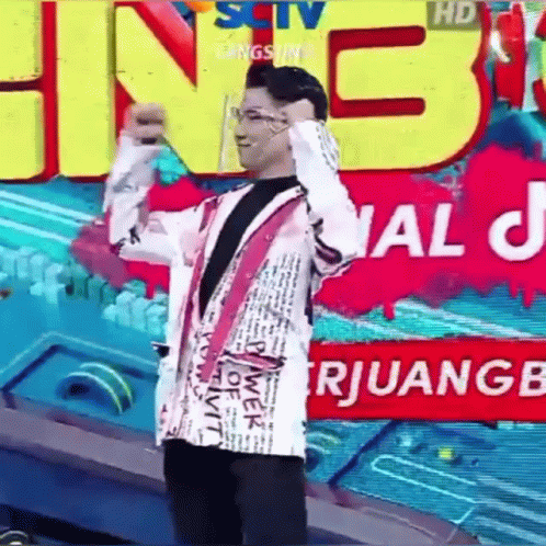 A Man In A White Jacket Is Standing In Front Of A Large Sign That Says ' Sctv ' On It . GIF