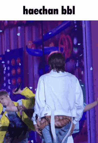 A Man In A White Jacket Is Standing In Front Of A Purple Wall With The Words Haechan Bbl Written Above Him GIF