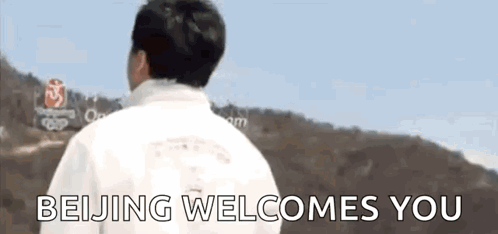 A Man In A White Jacket Is Standing In Front Of A Sign That Says Beijing Welcomes You . GIF