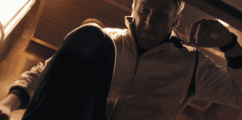 A Man In A White Jacket Sits On The Floor Looking Down GIF