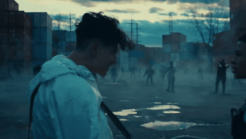 A Man In A White Jacket Stands In Front Of A Crowd Of People GIF