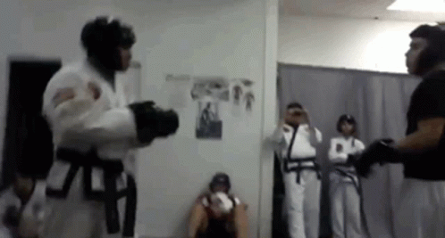 A Man In A White Karate Uniform Is Fighting Another Man In A Black Belt In A Room . GIF