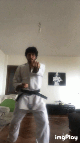 A Man In A White Karate Uniform With A Black Belt Is Doing A Karate Stance GIF