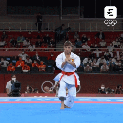 A Man In A White Karate Uniform With A Red Belt Performs A Karate Move In Front Of A Crowd At The Olympics GIF