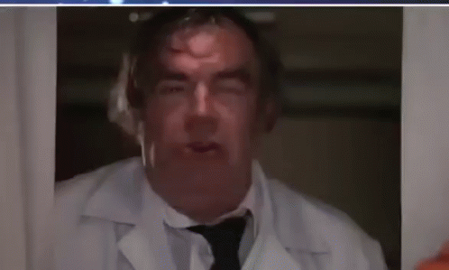 A Man In A White Lab Coat And Tie Is Looking Out A Window . GIF