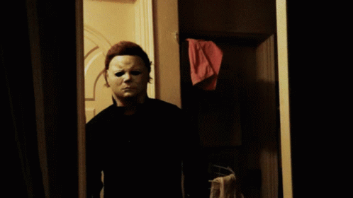 a man in a white mask is standing in a doorway holding a knife