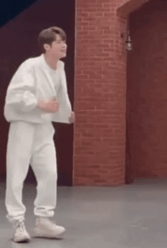 A Man In A White Outfit Is Dancing In Front Of A Brick Wall . GIF