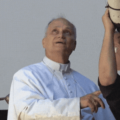 A Man In A White Robe Is Holding A Hat In His Hand GIF