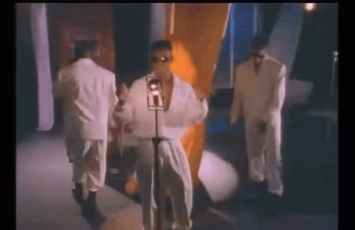 A Man In A White Robe Is Singing Into A Microphone While Standing Next To Two Other Men In Suits . GIF