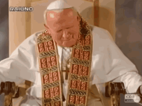 A Man In A White Robe Is Sitting In A Chair With A Cbs Logo Behind Him GIF