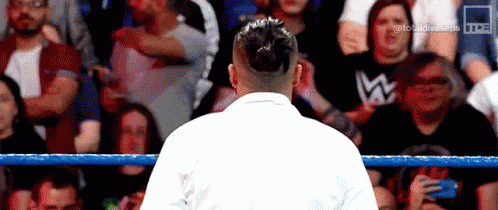 A Man In A White Robe Is Standing In A Wrestling Ring . GIF