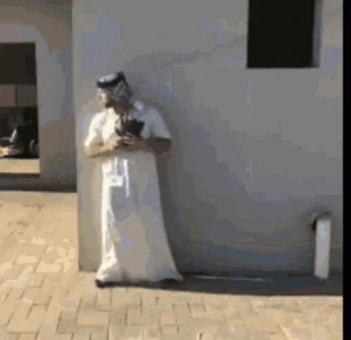 A Man In A White Robe Is Standing Next To A Wall GIF