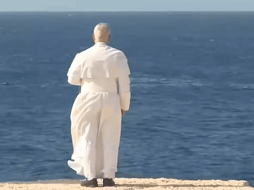 A Man In A White Robe Is Standing On A Cliff Overlooking A Body Of Water GIF