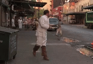 A Man In A White Robe Is Walking Down A Street GIF