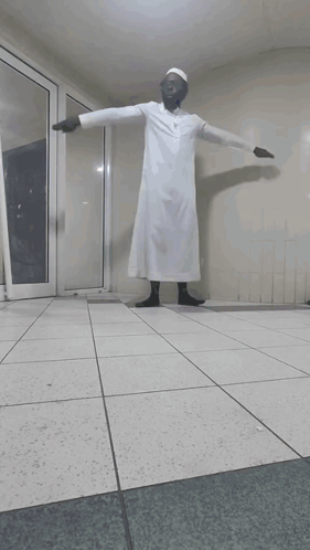 A Man In A White Robe Stands In A Hallway GIF