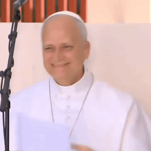 A Man In A White Robe Stands In Front Of A Microphone Smiling GIF